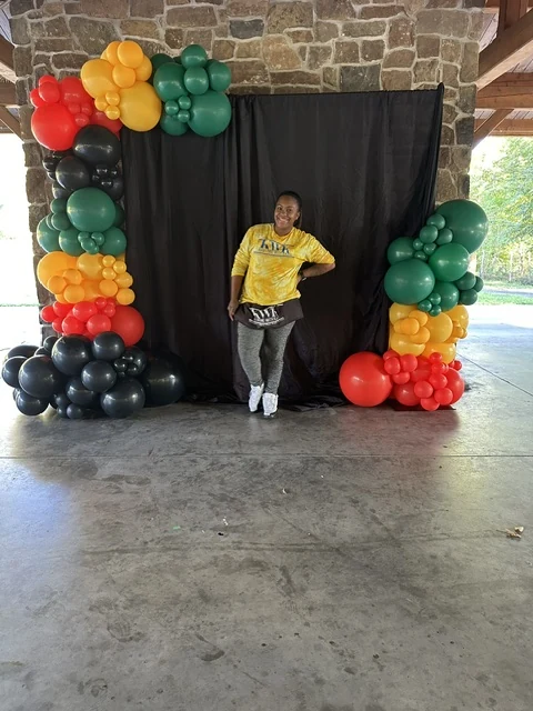 Kasia standing in front of her colorful red, yellow, green and black balloon installation